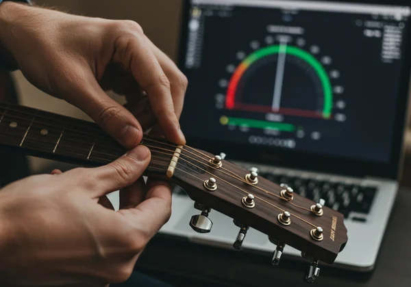 Hands tuning a guitar with an online tuner on a screen.